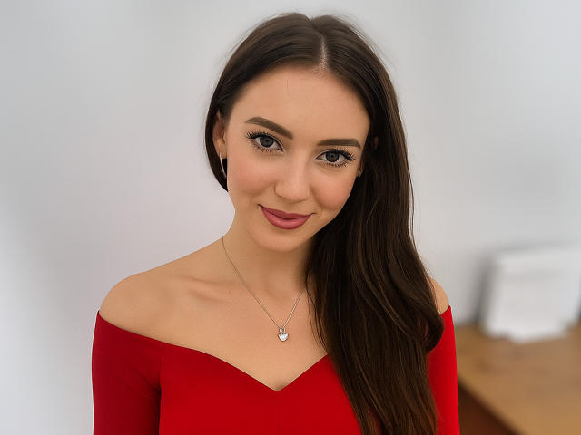 HarperSensitive with long brown hair, red off-shoulder top, small heart necklace, and subtle smile, showing her tits and ass in a photo. She's pretty and has a cute face.