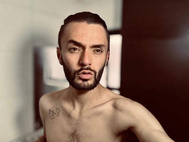 JakeMagnus, shirtless, with a trimmed beard, short dark hair, tattoo on right chest, looking at camera, slightly wet skin, brown eyes, dark eyebrows, medium build, attractive.