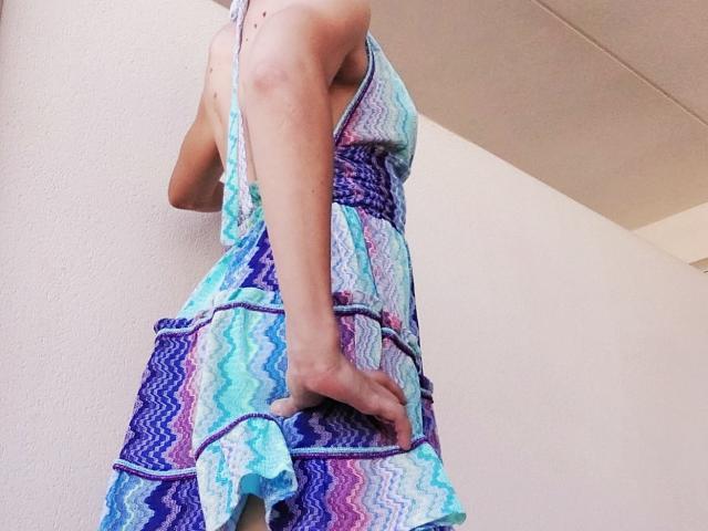 OrianaLaFrancaise in a colorful, zigzag-patterned dress, holding her ass with one hand, showing her back and side, in a low-angle shot.