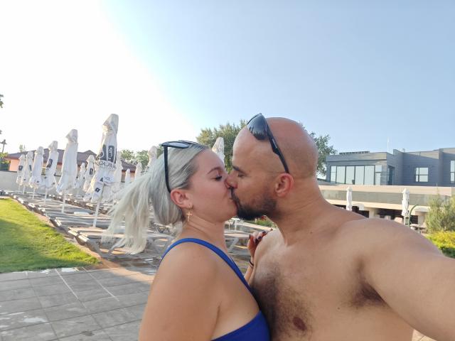 La testa di CandyHotCouple69, con un cappello blu e un cappello rosso parzialmente visibile sopra un muro grigio, sullo sfondo di un cielo blu limpido..