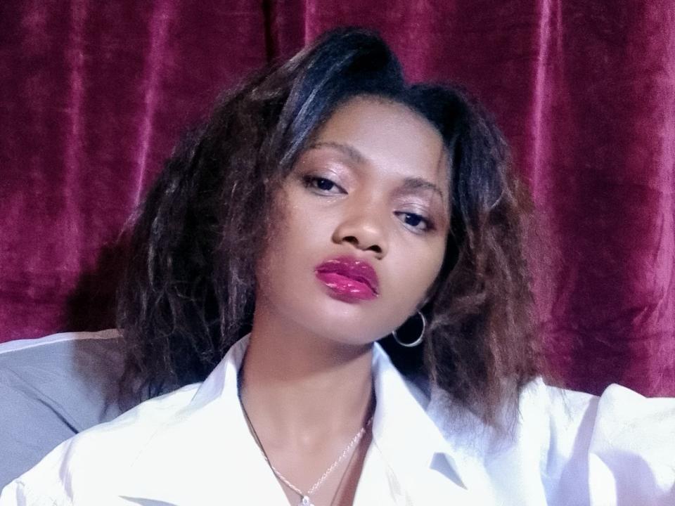 Cassiy has dark, wavy hair, purple lipstick, hoop earrings, and a white shirt, looking serious with a slight pout. Her ass is not visible. Red curtain background.