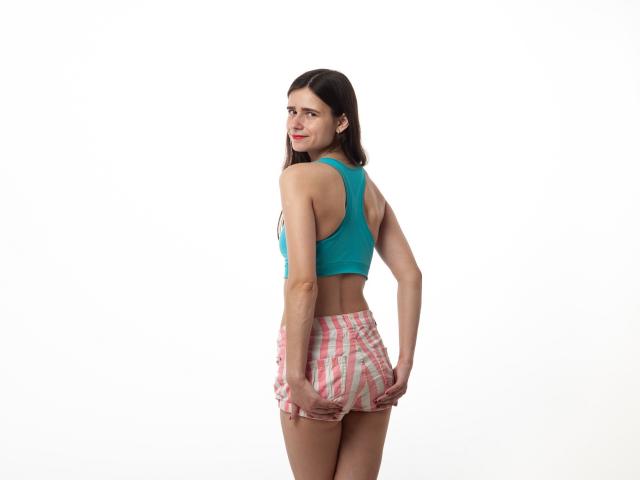 MartaLeee with dark hair, teal sports bra, and pink striped shorts, smiling back, hands on her ass, white background.
