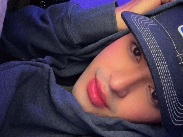JustinStone has pink lips, brown eyes, and a blue hat with white lines, wearing a blue hoodie, lying down with arms above his head.