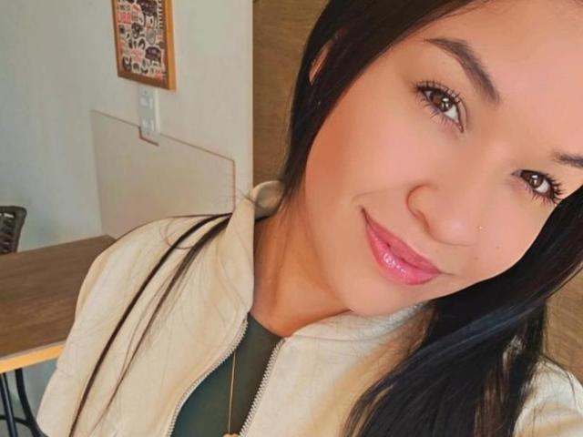 FerryNanda with shiny pink lips, black hair, brown eyes, and a slight smile, wearing a white jacket over a green shirt, has a cute nose and small nostrils.