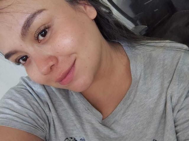 A MartinaMarX tem um rosto adorável, ligeiramente convencido, pele clara, olhos castanhos, nariz pequeno e um sorriso gentil. Ela está vestindo uma camiseta cinza com decote em V, e tem cabelo escuro..