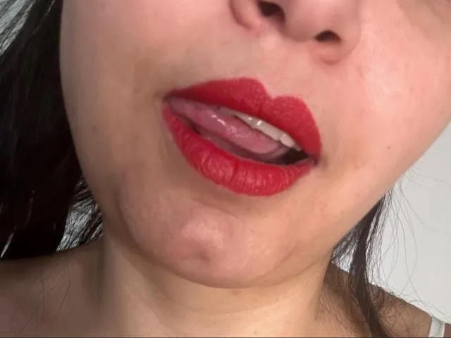 SweetMaryHot69's face with red lipstick, tongue slightly out, showing a bit of white teeth, and her chin's soft skin. Her dark hair is barely visible.