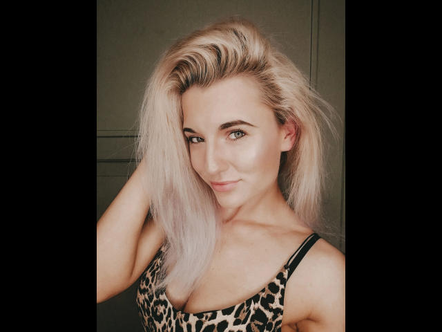 JayJayPink-hot with platinum blonde hair, green eyes, and a confident smirk, wearing a leopard print top, showing her tits and a cute, sexy face.