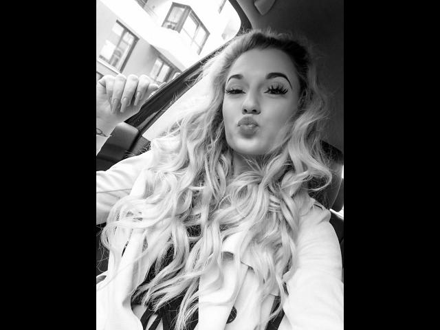 JayJayPink-hot with long, wavy blonde hair, pouty lips, and thick eyelashes, sitting in a car, holding the door with a sexy, confident look in a black-and-white photo.