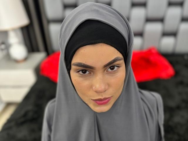 HotMalatha with a gray hijab and black undercap, brown eyes, pink lips, and a nose ring, looking directly at the camera. Her ass is not visible.