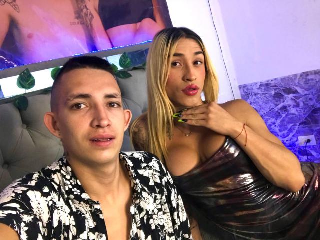 MyaAndJack69 with blonde hair, pouty lips, and shiny black dress, next to Jack with short hair, black floral shirt, and visible chest tattoos, in a club setting.