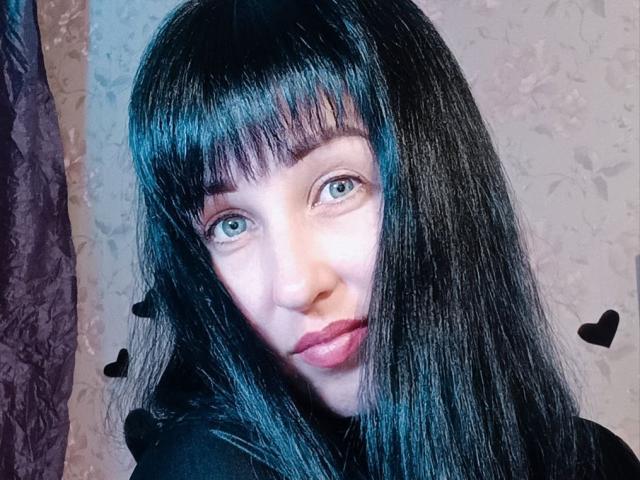 JillSilvies has black, straight, shiny hair with bangs, blue eyes, and pink lips, wearing a black hoodie, with small black hearts on the right side.