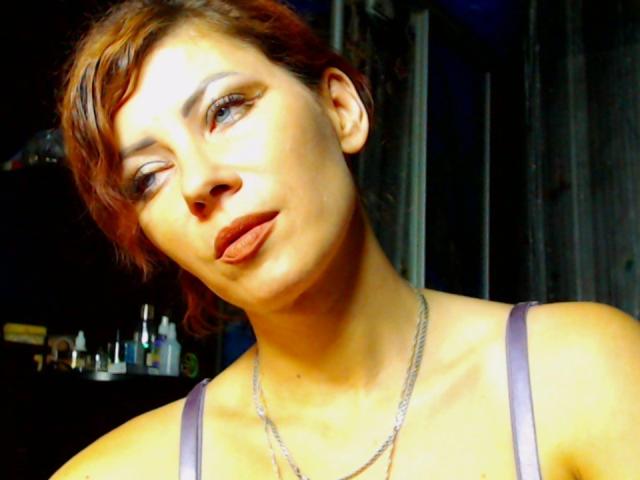 JuliaIce has short brown hair, pouty lips, and a slight tilt of her head. She's wearing a purple tank top with a silver necklace, looking off to the side.
