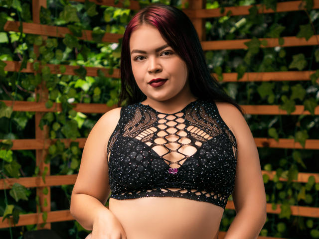 CharlottexEvans has dark red hair, black lace bra with pink bow, and is looking at the camera with a slight smile, showing her tits and a bit of her ass.