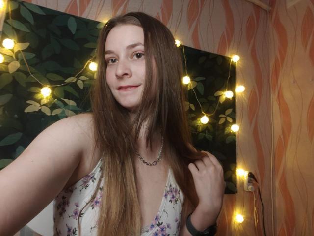 LunaBliss69 with long brown hair, small tits, wearing a floral dress, holding hair, smiling, fairy lights, necklace, soft pink wallpaper, warm yellow lights in the background.