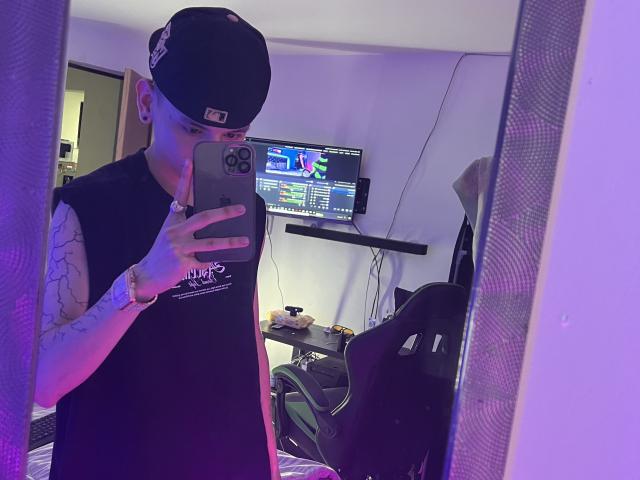 HardinBat with tattoos, black beanie, sleeveless black shirt, holding phone in mirror selfie, purple lighting, gaming chair, TV on wall, phone case with camera, wristwatch.