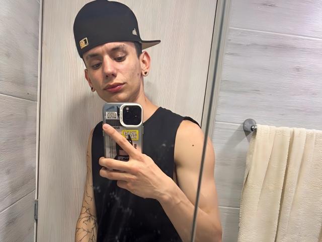 HardinBat, wearing a black cap and sleeveless shirt, takes a mirror selfie with a phone, showing a tattoo on his right arm and a nose ring.