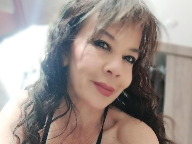 SamaraBellet has wavy brown hair, dark eyeliner, and pink lipstick. She's smiling with a black halter top, showing her bare shoulders and a hint of her breasts.