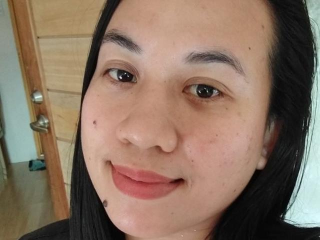 SexyHotLuna69 has a cute face with black hair, light skin, brown eyes, and a small smile. She has a few moles and is wearing pinkish lipstick.