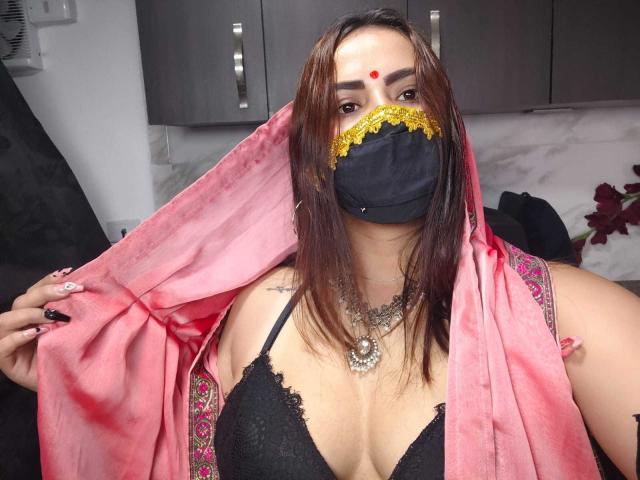 Dalia Dubey, met bruin haar, een zwarte kanten bh, een roze sari, en een gouden masker, die haar borsten laat zien, draagt een rode bindi en meerdere kettingen, op een selfie..