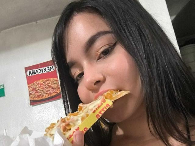 LissyCarter with long black hair, eating a slice of pizza with cheesy crust, her eyes half-closed, mouth full, and a small nose piercing visible.