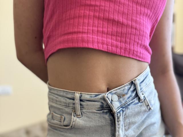 SofiVernara's pink ribbed crop top, showing her toned midriff, and light blue, unbuttoned, high-waisted jeans with visible button hole.