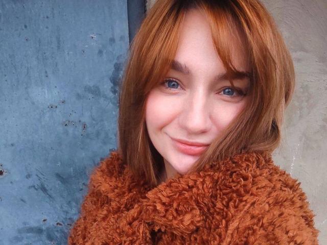 ArinaWinss with red hair, blue eyes, and a cute smile, wearing a fluffy brown sweater, has a soft, sexy face. Her tits are not visible, just her face.