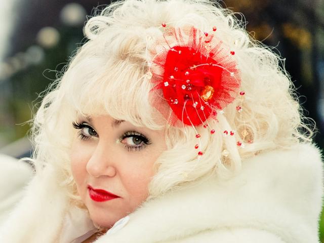 MilfLana with curly white hair, red flower hairpiece, and red lipstick, wearing a white fur coat, has a sexy, cute, and attractive look with her large, dark eyes.
