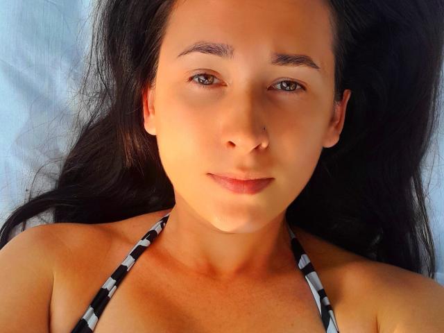 RareLazery has tan skin, dark brown eyes, and long black hair. She's wearing a black-and-white striped halter top, with small boobs visible. She has a nose ring.