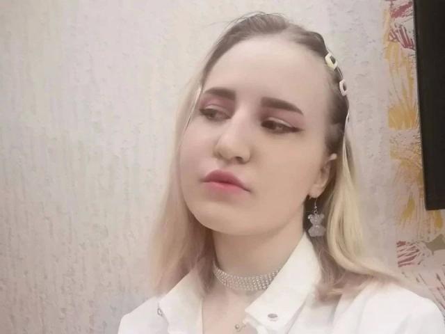 AngelOfGrom-hot with pale skin, blonde hair, pink eyeliner, pink lipstick, white shirt, choker, earrings, and a slightly bored expression.