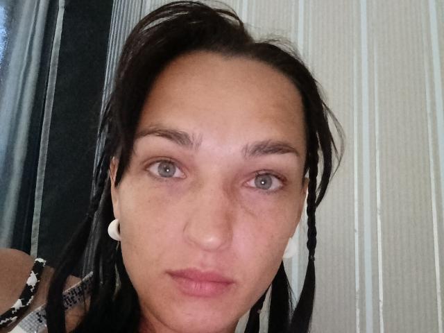 MagsieFrancy heeft bleke huid, blauwe ogen en zwarte dreadlocks, draagt witte oorbelletjes, heeft een neutrale uitdrukking en lichtroze lippen, en kijkt recht in de camera..