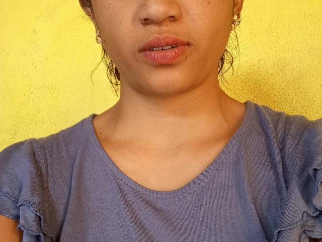 Tann69's face with pinkish lips, small nose, light brown skin, wearing a blue shirt, earrings, and wet curly hair. Yellow background. Boobs not visible.