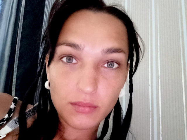 Le visage de MagsieFrancy, montrant ses yeux marrons, ses cheveux noirs et ses écouteurs blancs, avec ses lèvres roses légèrement entrouvertes. Elle regarde directement l'appareil photo avec une expression neutre..