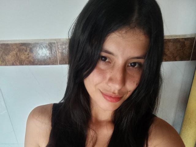 MadissonFontaine has long black hair, brown eyes, and a slight smile. She's wearing a black sleeveless top, showing her bare shoulders. Her skin is light with a few freckles.