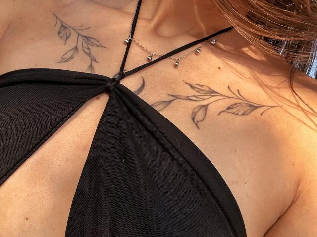 Karish's black halter top shows her tits with a leaf tattoo on each side of her chest. Her neck has a silver chain with small balls.