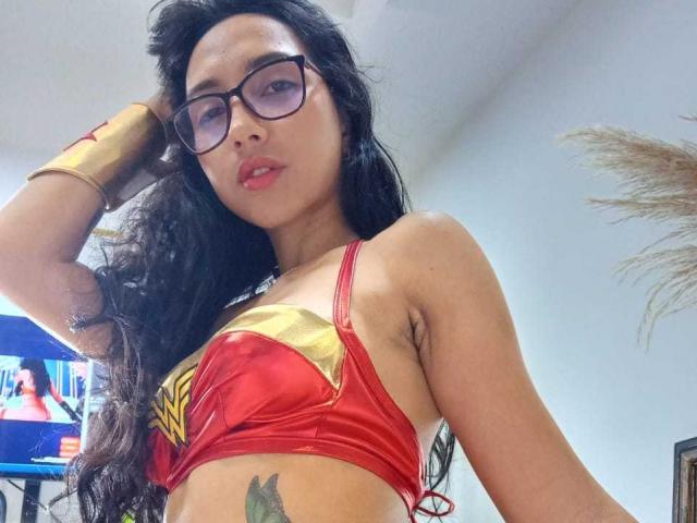 SofiaaMiiller with long black hair, glasses, red Wonder Woman bikini top, gold bracelet, and a tattoo on her right side, looking at the camera with a slight smile.