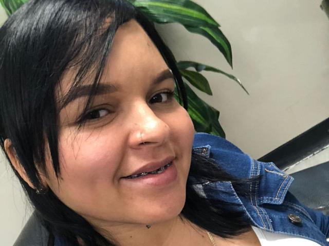 YeriBellani has black hair, a nose ring, and a denim jacket, smiling with black metal teeth, showing a small heart tattoo below her chin.