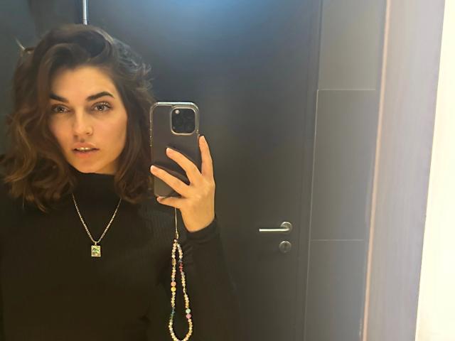 LuciaLove-hot with curly brown hair, wearing a black turtleneck and gold necklace, taking a mirror selfie, showing her ass in the reflection, holding a phone with a colorful strap.