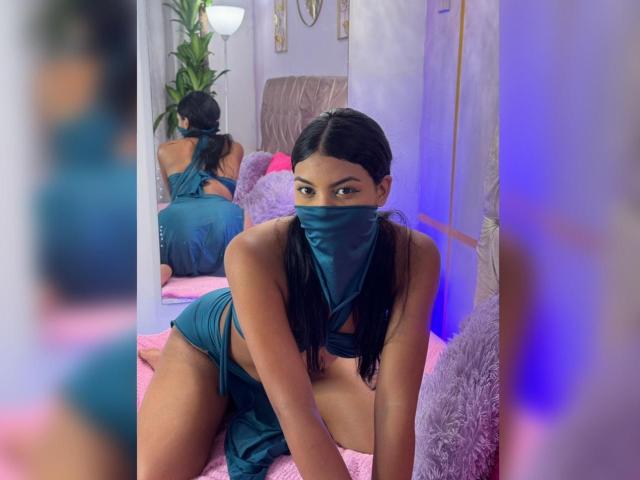 LalilaBrunette with dark hair in pigtails, teal mask, and matching teal lingerie, on knees, showing her tits and ass, reflected in mirror, purple and pink room.