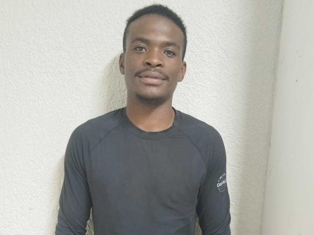 ThrobingDickZa is a dark-skinned dude with short curly hair, a mustache, and a slight smile. He's wearing a black long-sleeve shirt against a white textured wall.