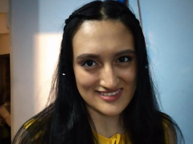 CarolineHarpper has long black hair, dark eyes, and a cute smile. She's wearing a yellow top with a bow, and has small tits. Her skin is light brown.