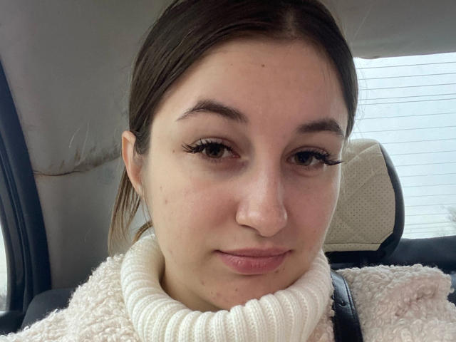 RonixHofma a un visage mignon, avec une peau claire, des yeux marron et de longues cils noirs. Elle porte un pull blanc à col roulé texturé et est assise dans une voiture..