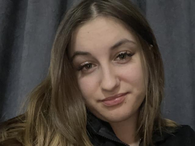RonixHofma a les cheveux brun clair, un maquillage discret, et un léger sourire avec une petite imperfection sur sa joue droite. Elle porte une veste noire. Elle a une apparence mignonne et décontractée..
