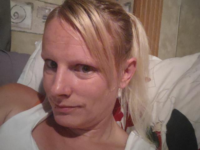 KaszyMarie has blonde hair in a ponytail, light skin, small nose, and is wearing a white top with red floral patterns, looking at the camera with a slight smile.