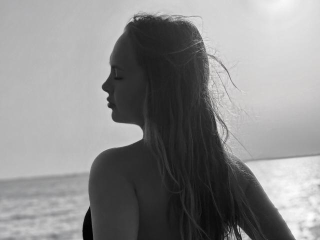 Black-and-white photo of KhaleesiMoon with long, wet, and slightly tangled hair, facing side with closed eyes, showing bare shoulders and a subtle silhouette of her tits.