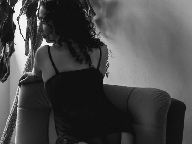 Samantha Antolín, con cabello negro y rizado, de espaldas a la cámara, vestida con un top negro de tirantes finos y pantalones ajustados, apoyada en una silla, con las nalgas ligeramente levantadas, fotografía en blanco y negro..