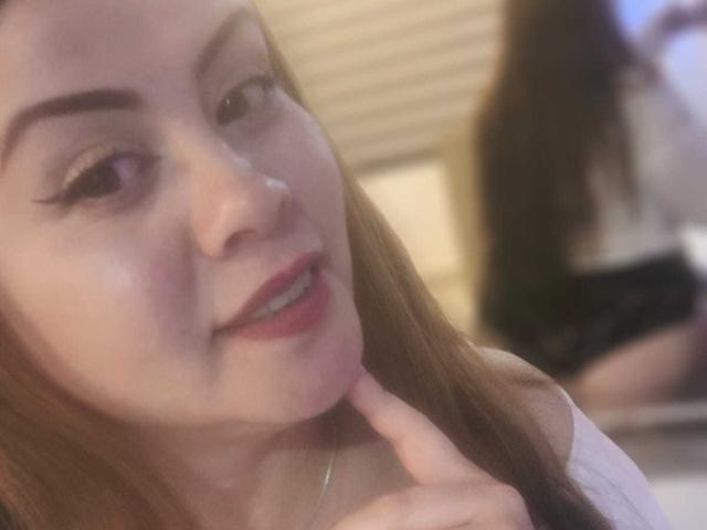 AstridBayon ha un sorriso carino, con rossetto rosa, sopracciglia marroni e lunghi capelli castani. Si tocca il mento con un dito, mettendo in mostra il suo piccolo naso..