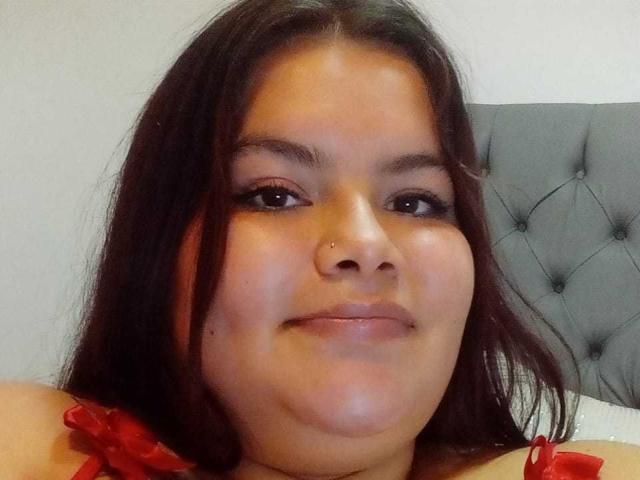 CelesteSoler has brown eyes, a nose piercing, and a slight smile. She's wearing a red top with straps, and her dark hair is straight and loose.