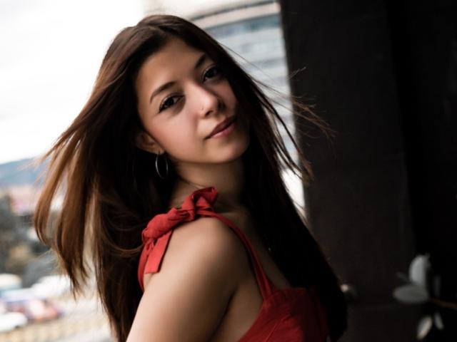 CloeMiiller with long brown hair, red dress, and hoop earrings, looking over shoulder with a slight smile, soft light, slightly blurred background, casual, confident, cute.