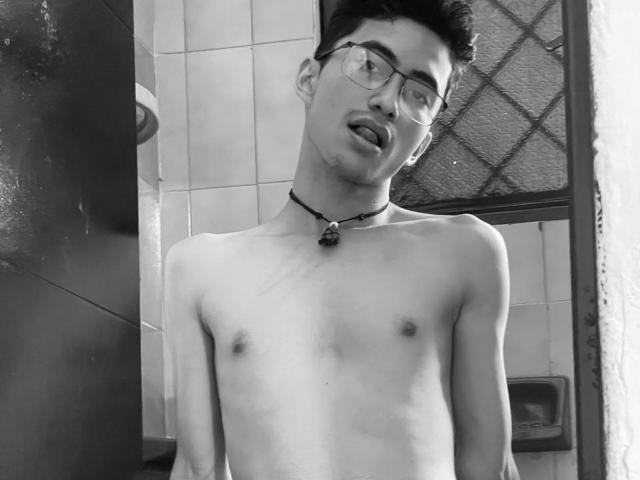 AnryuOswald, shirtless, with glasses, short dark hair, necklace, tongue out, small nipples, slim, in black-and-white, bathroom setting, medium shot, front view, slightly messy look.