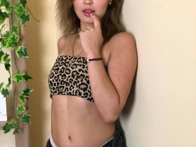 SofiVernara con un top sin tirantes de estampado de leopardo, con un dedo en la boca, labios rosados, cabello castaño, una pulsera y jeans, mostrando su abdomen plano y trasero pequeño..